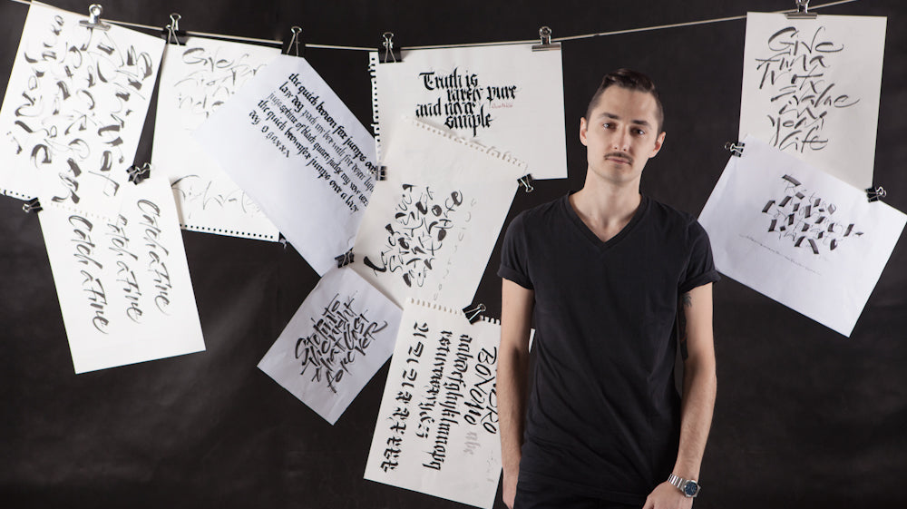 Sandro the artist stands in front of a black background with this work hung on a washing line and pegs behind him