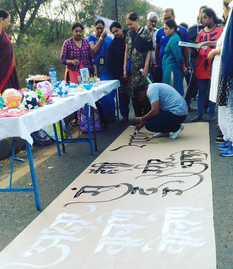 A calligrapher kneels on the floor while drawing some street art as a crowd looks on.