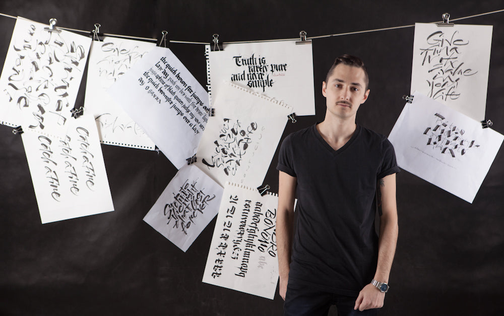 Sandro the artist stands in front of a black background with this work hung on a washing line and pegs behind him