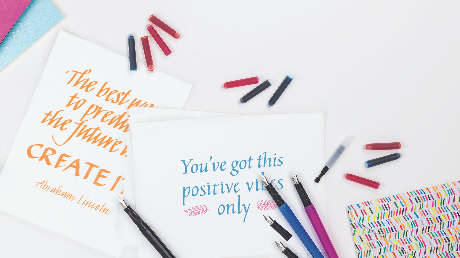 A lifestyle image of pens and ink cartridges on a clean white desk, a piece of calligraphy reads "You've got this positive vibes only"