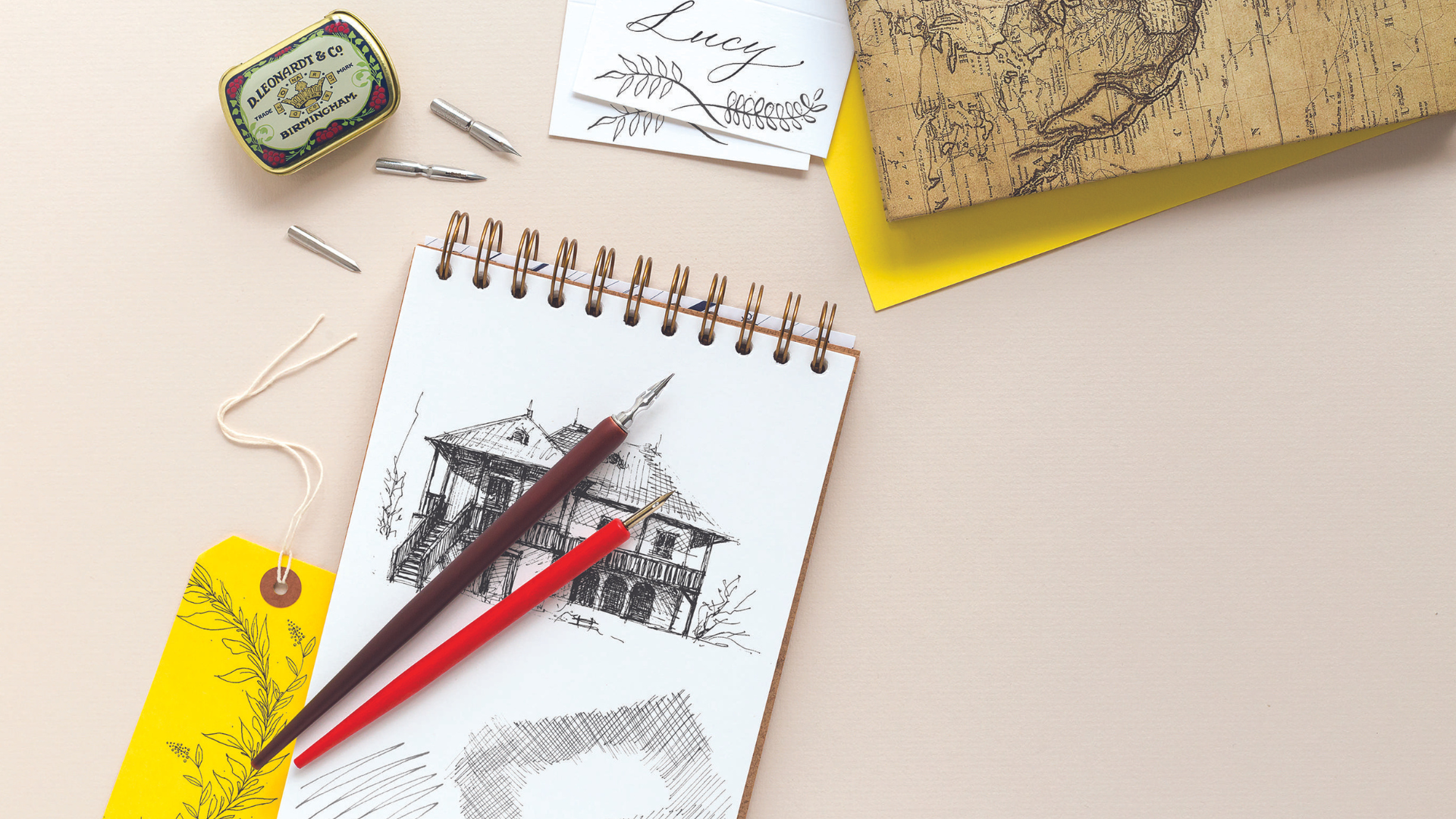 A lifestyle shot of nibs and dip pens arranged on a desk with drawings and calligraphy.