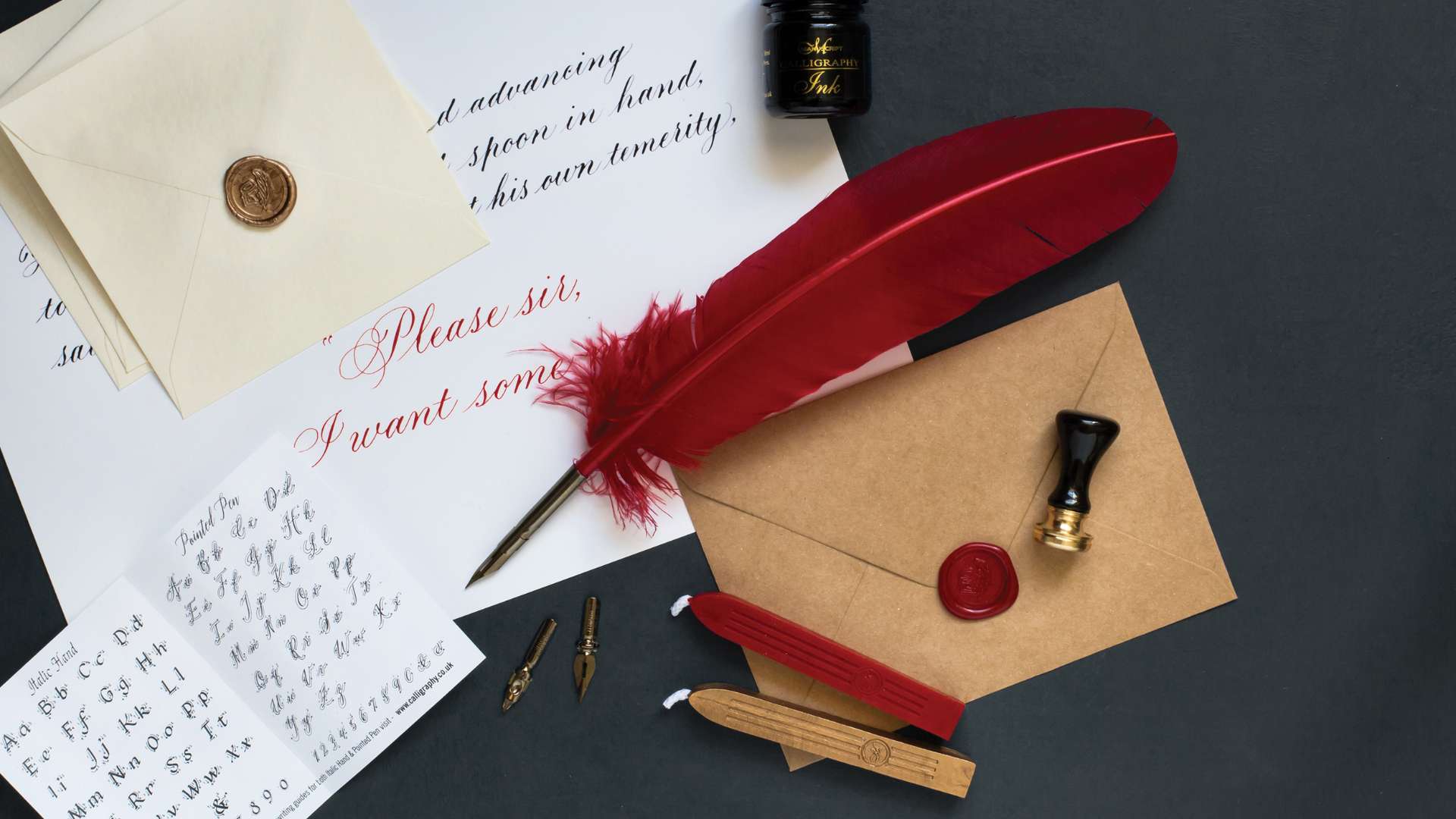 A lifestyle layout of heritage products on a grey background including: a red quill, a brown envelope, wax wick sticks, and inks.