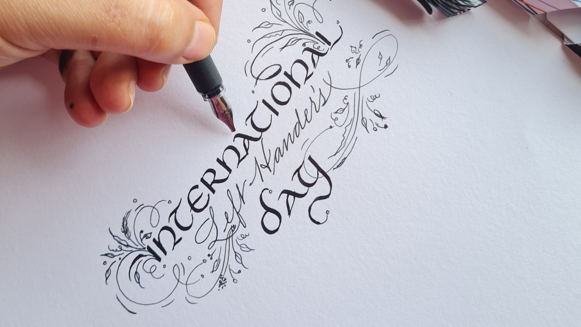 "International left handers day" is written in beautiful calligraphy script, while a hand hovers a clarity fountain pen above. 