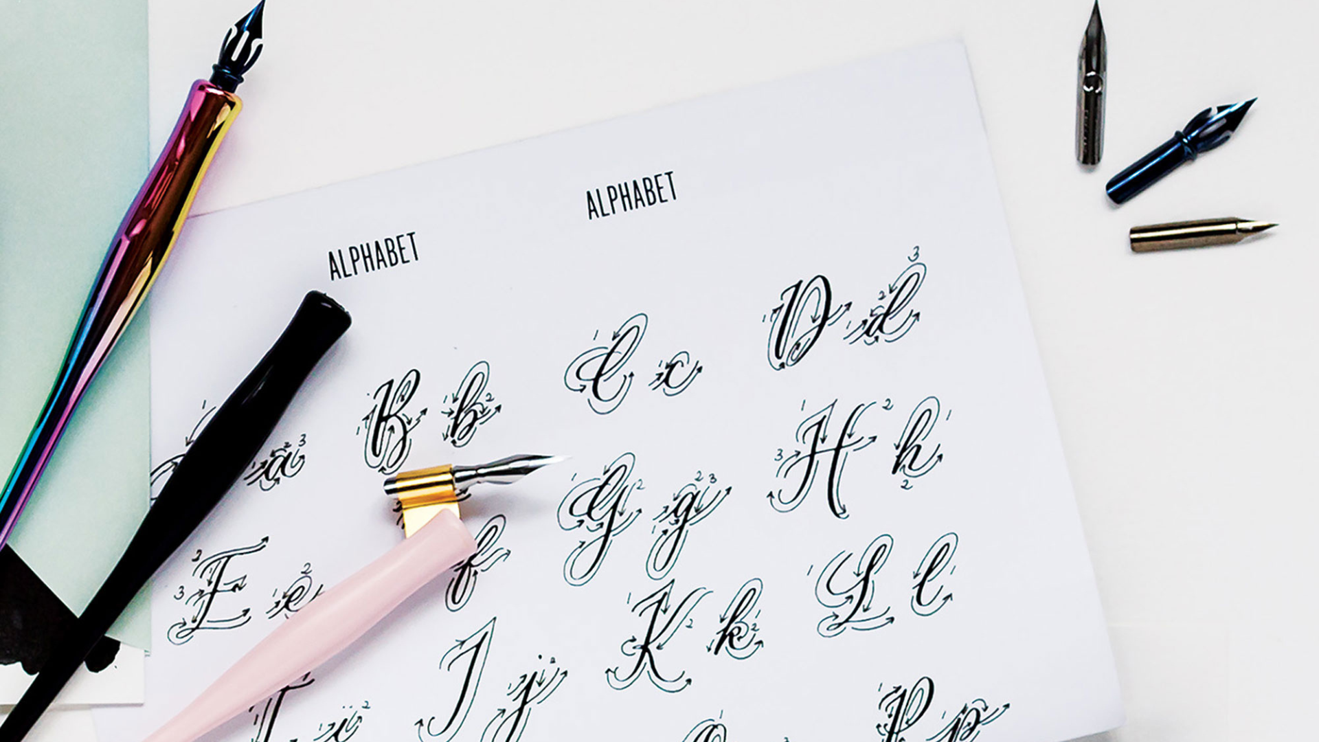 Calligraphy alphabet sheet with writing instruments on a light background