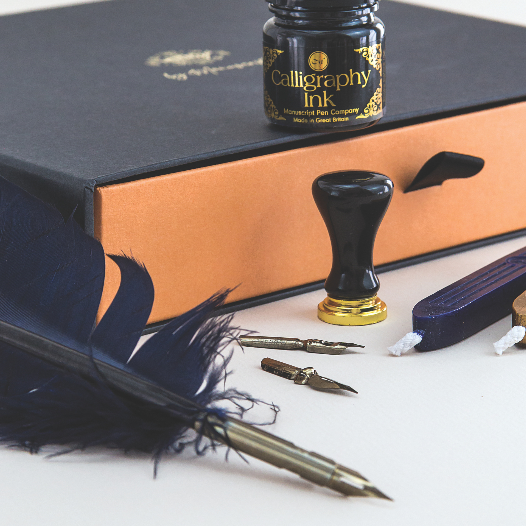 Calligraphy set with ink bottle, feather pen, and inkwell on a white surface