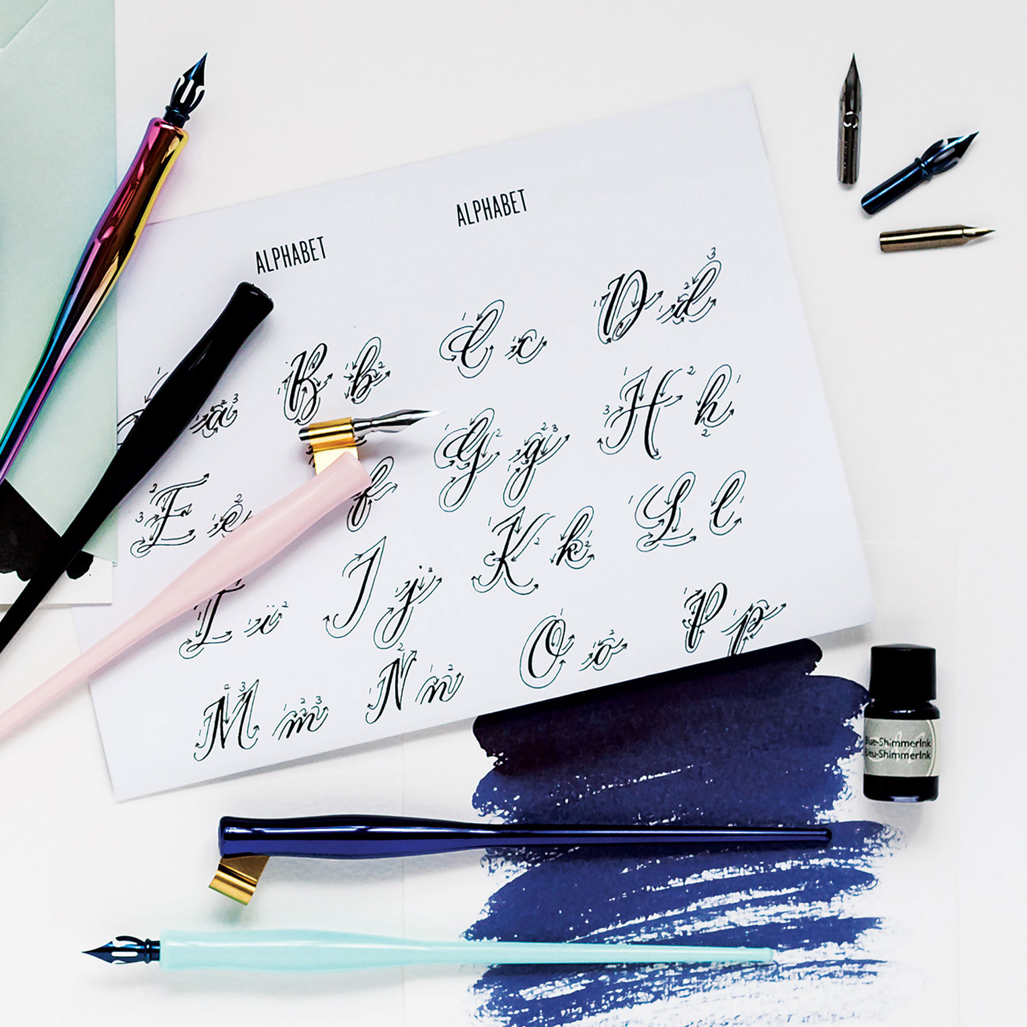 Calligraphy practice sheet with fountain pens and ink bottle on a white background