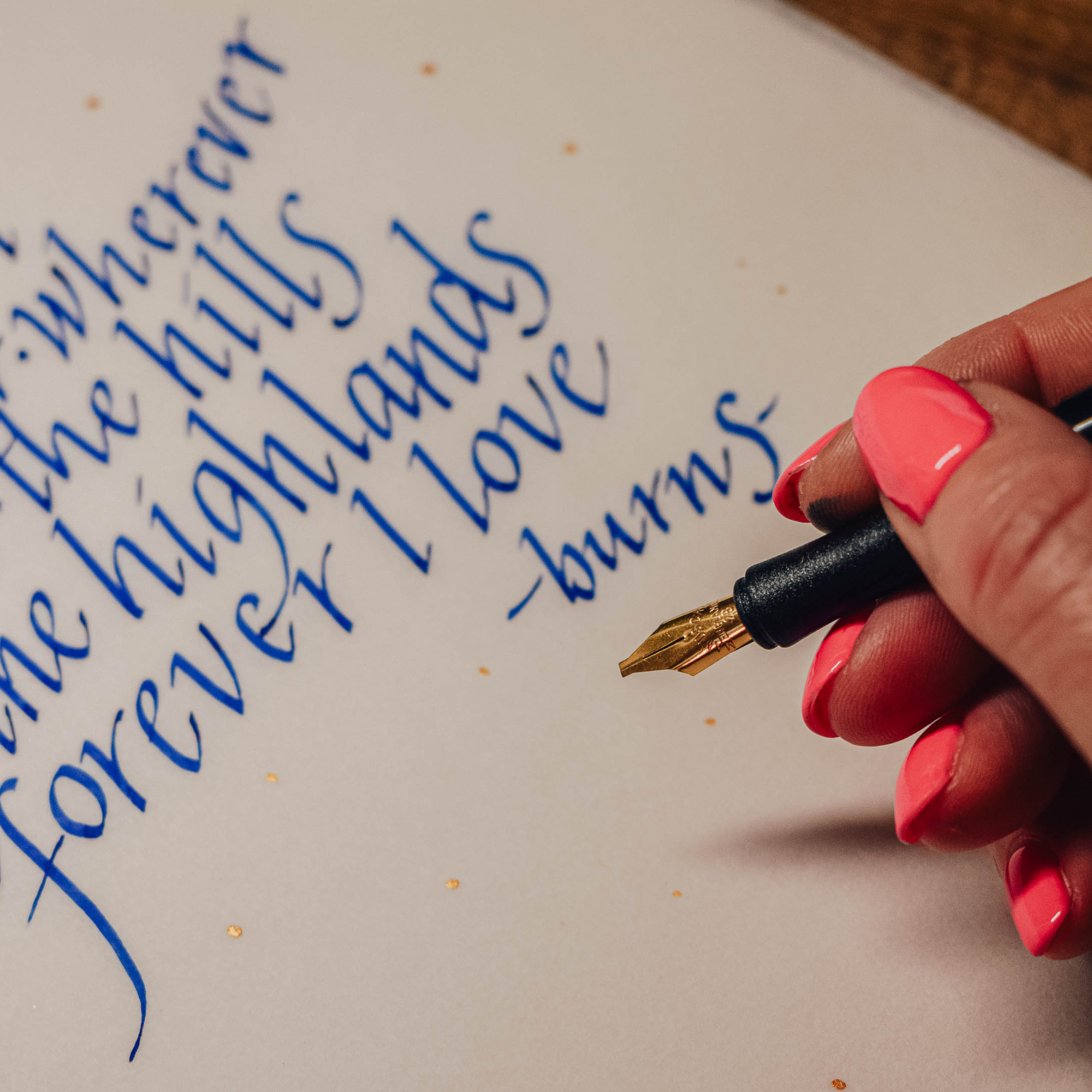 Hand with pink nail polish holding a fountain pen over handwritten text on paper